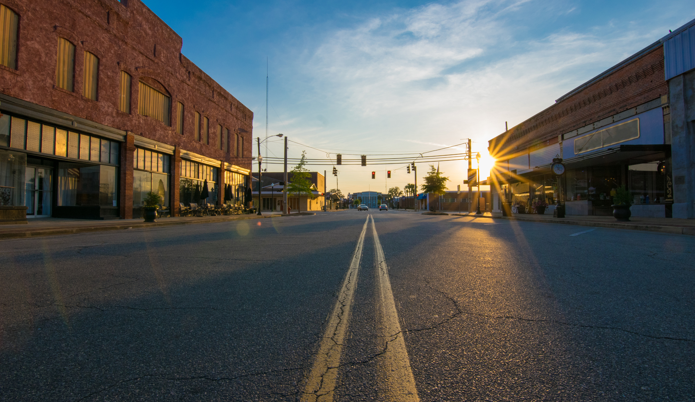 Storefronts at sunset in the middle of the road in downtown in a small town. The street and parking spaces are empty.